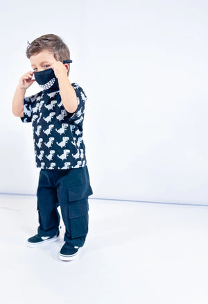 Child wearing a black Little Aurel t-shirt with white dinosaur print and black cargo pants on a white background