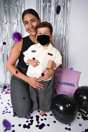 Woman holding a child in front of a silver curtain with black and purple balloons.