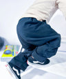 Person wearing black Little Aurel pants and a beige shirt on a light background