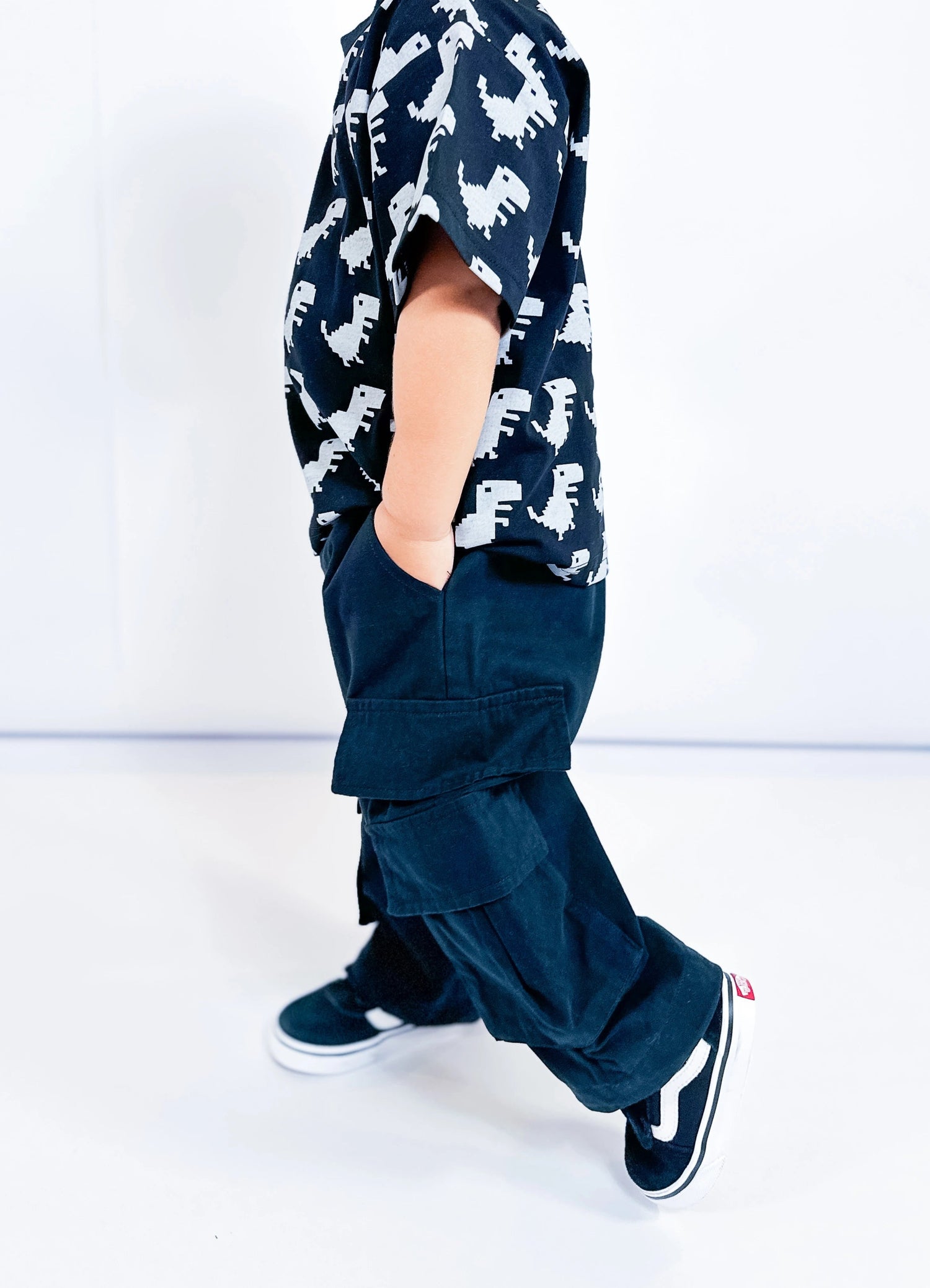 Child wearing a black shirt with dinosaur pattern and dark pants on a white background