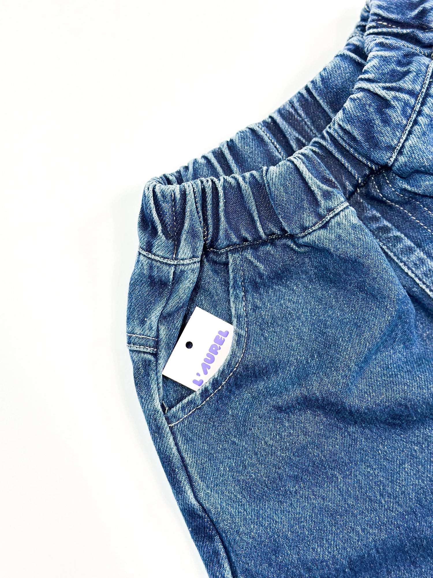 Close-up of blue denim pants with a brand tag on a white background
