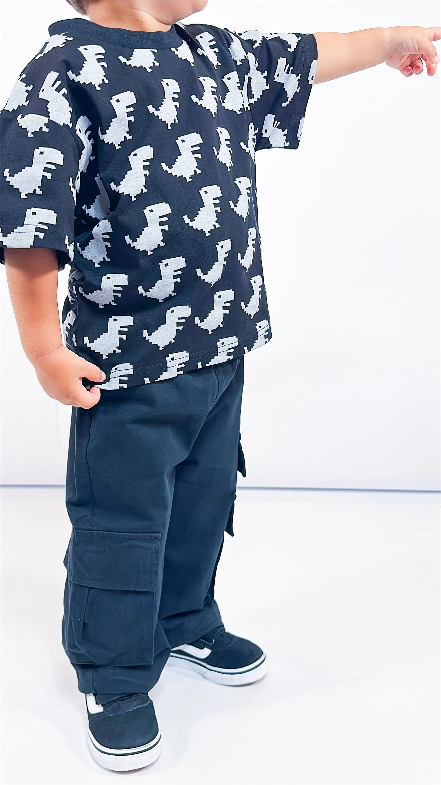 Child wearing a black Little Aurel t-shirt with dinosaur pattern and black cargo pants on a white background