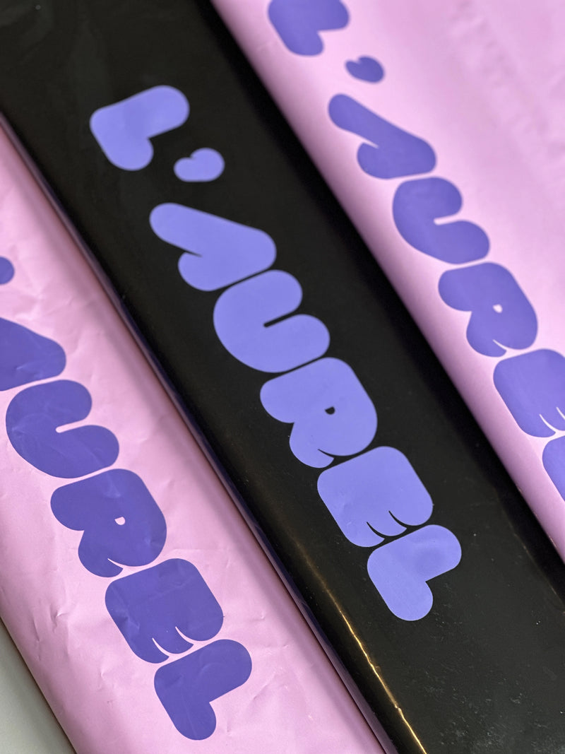 Three packaging with 'L'AUREL' branding in purple on a black, pink, and purple background.