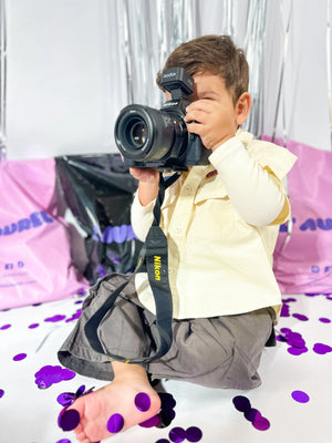 Model of Little Aurel holding a camerain front of a colorful background big Little Aurel packages.