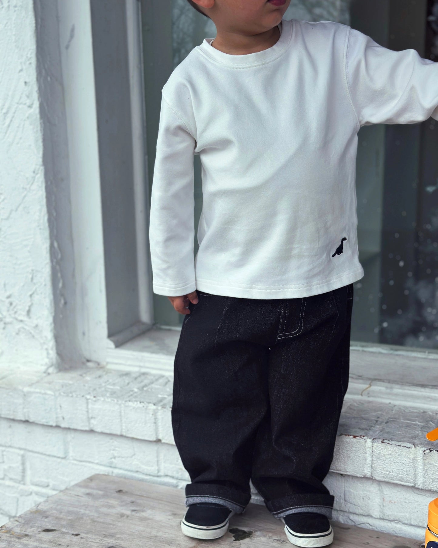 Child model wearing Loose-fit longsleeve shirt for kids in white with small dinosaur embroidery