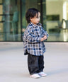 Child wearing a plaid shirt and dark pants standing on a sidewalk by Little Aurel