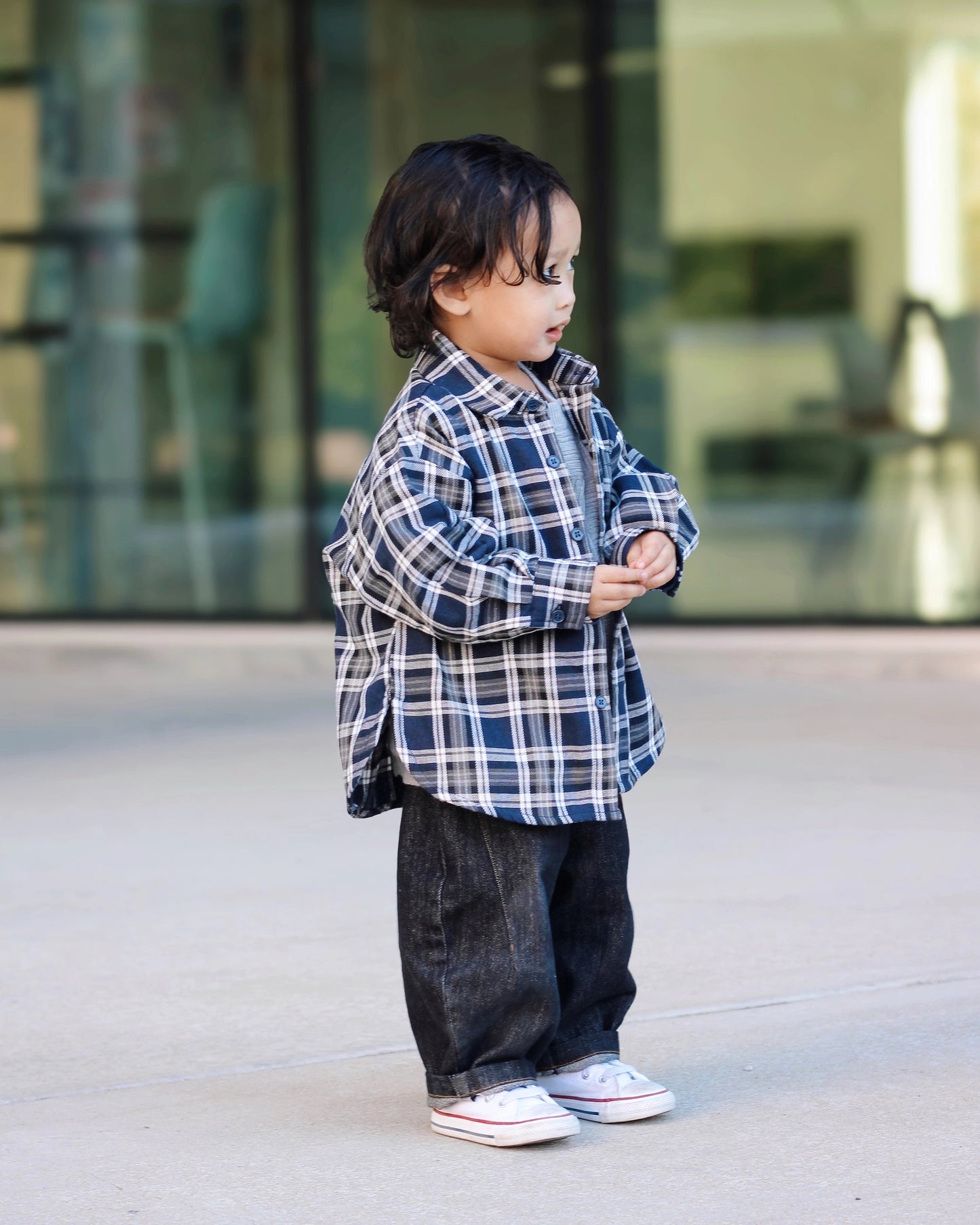 Child wearing a plaid shirt and dark pants standing on a sidewalk by Little Aurel