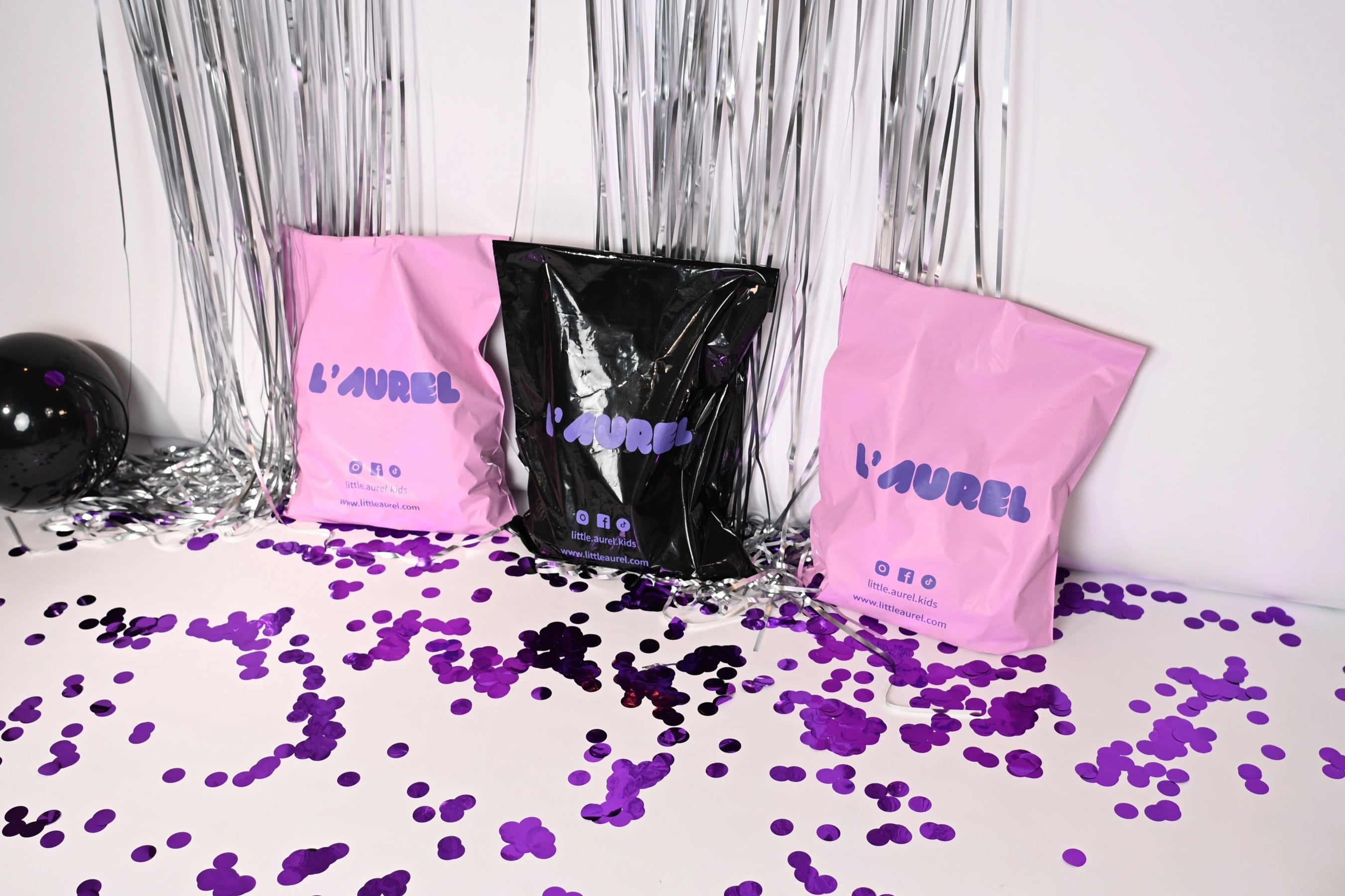 Party shoot setup with pink and black bags, purple confetti, and balloons on a white surface.