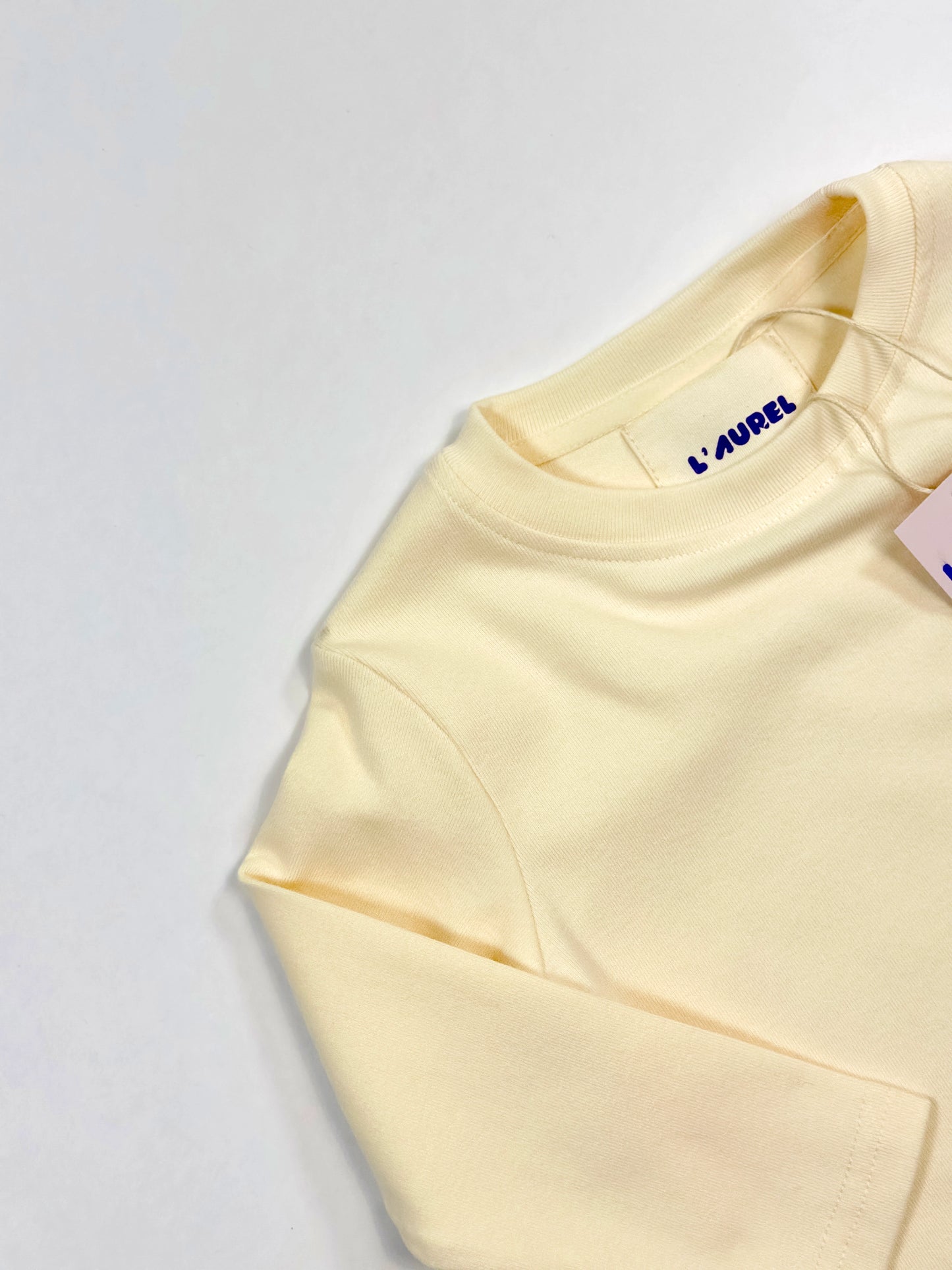 Light yellow sweatshirt with a brand tag on a light gray background by L'aurel