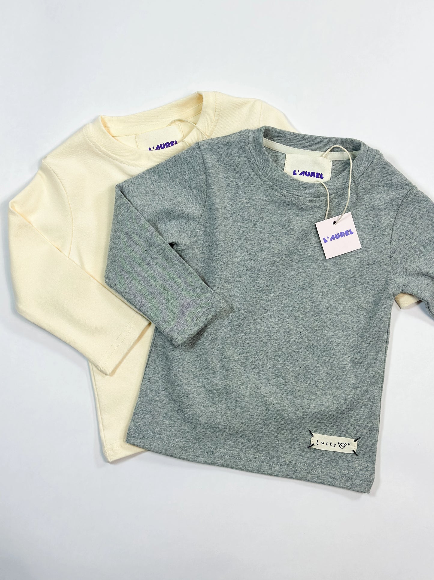 Two children's longsleeves, one beige and one gray, on a light gray background by L'aurel