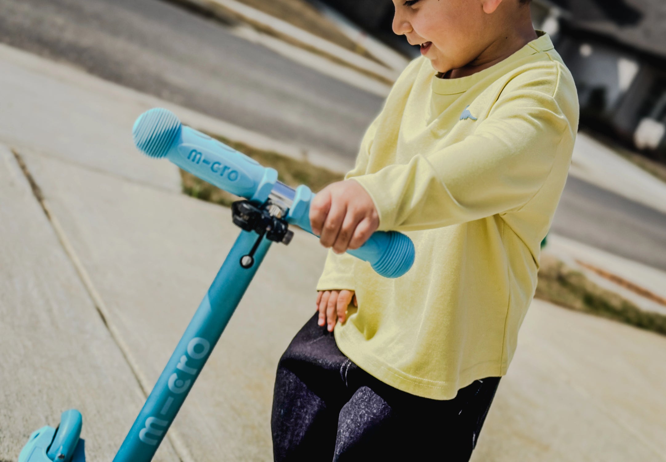 Child wearing graphic longlseeve from Little Aurel with a blue scooter on a sidewalk