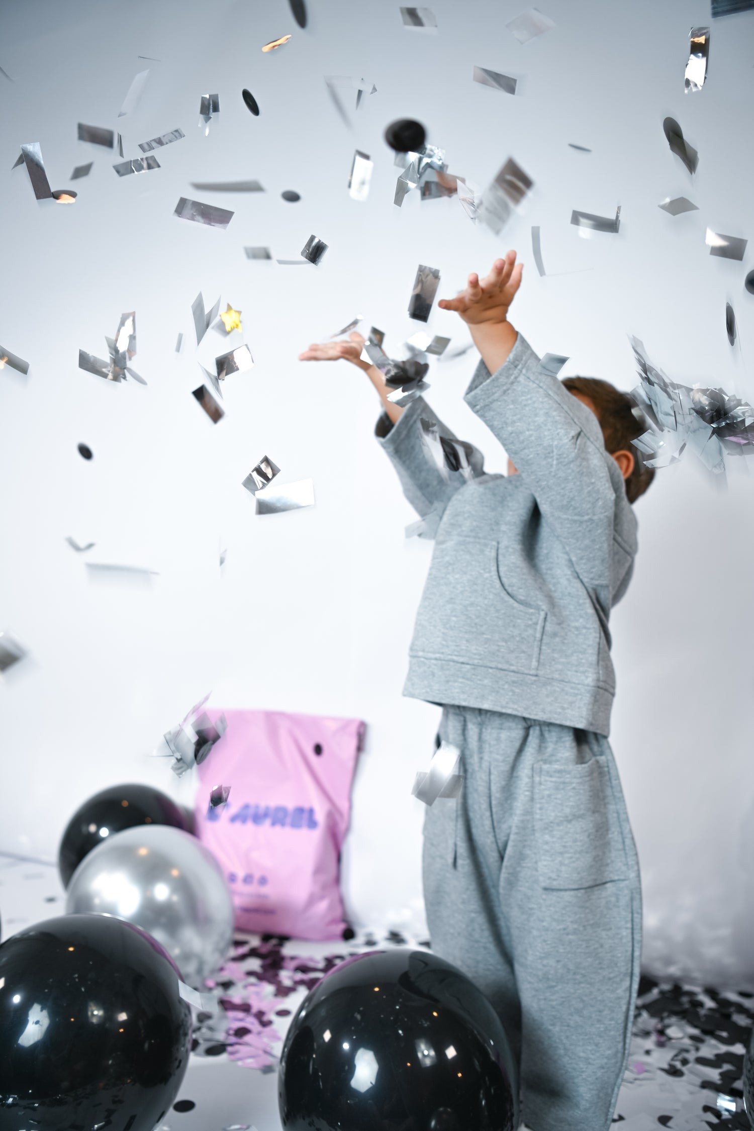 Little Aurel Model in gray sweater set with confetti and balloons in a celebratory setting